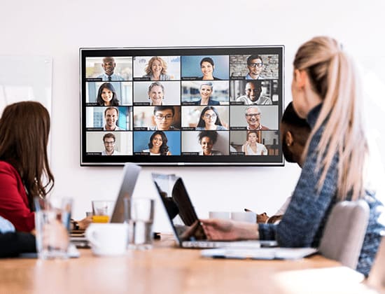 Les employés d'une salle de réunion regardent un écran avec une vidéoconférence en cours